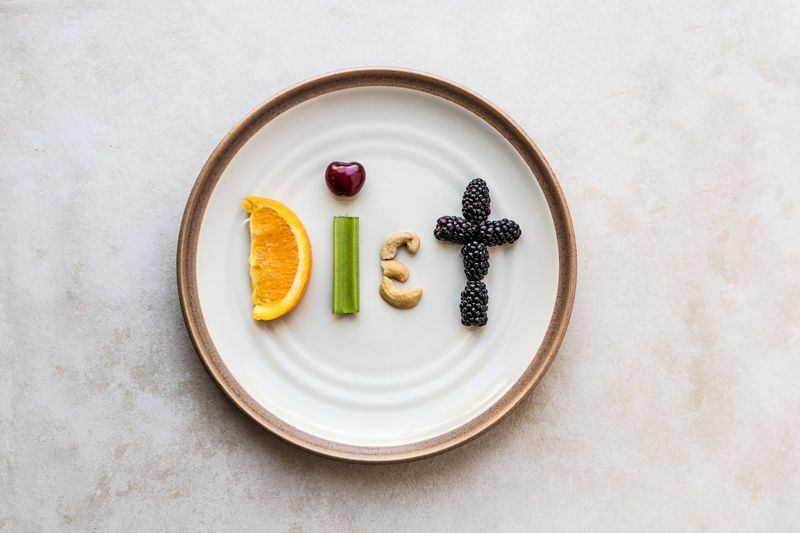 Ilustrasi diet The word Diet made from food. A orange slice, celery stick, cherry, cashew, and blackberry spell diet, as it sits on a stoneware plate. Using a flat lay over head view to capture the spelled out food word.