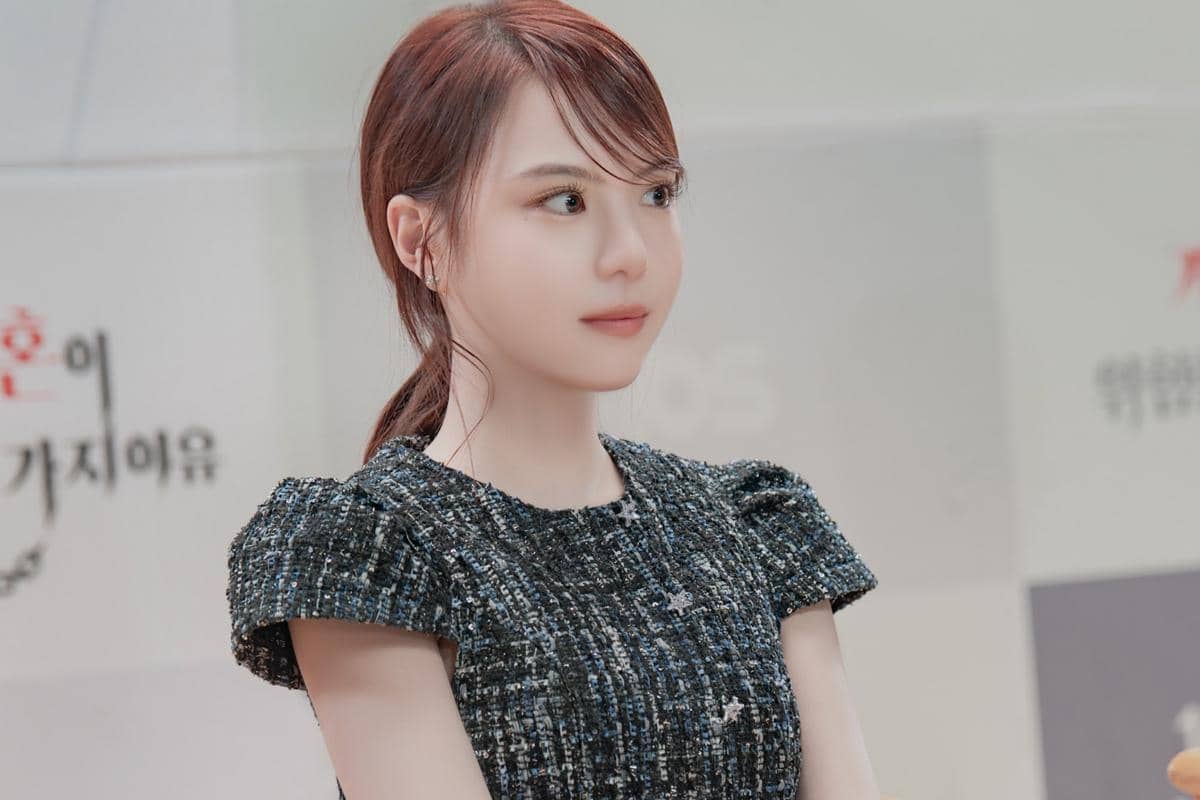 Seorang perempuan berambut cokelat mengenakan gaun bermotif biru gelap dengan latar bertulisan Korea dalam still cuts drama Dream to You.
