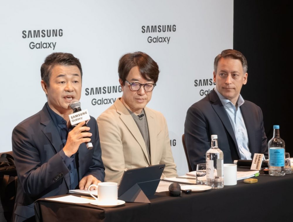 The image shows a group of people, possibly Samsung executives, gathered around a table with a Samsung Galaxy display, possibly for a product launch or presentation.